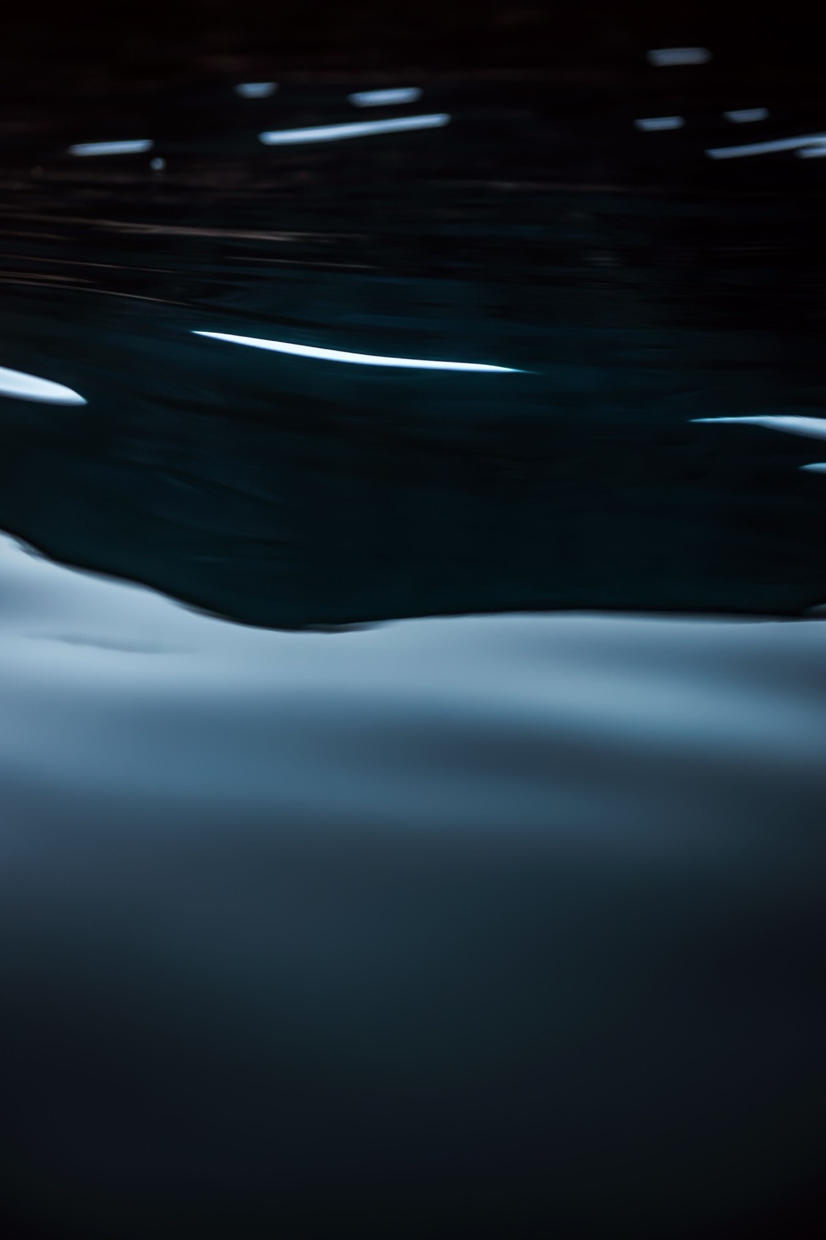 La surface d’une eau sombre et calme, traversée d’un trait de lumière.